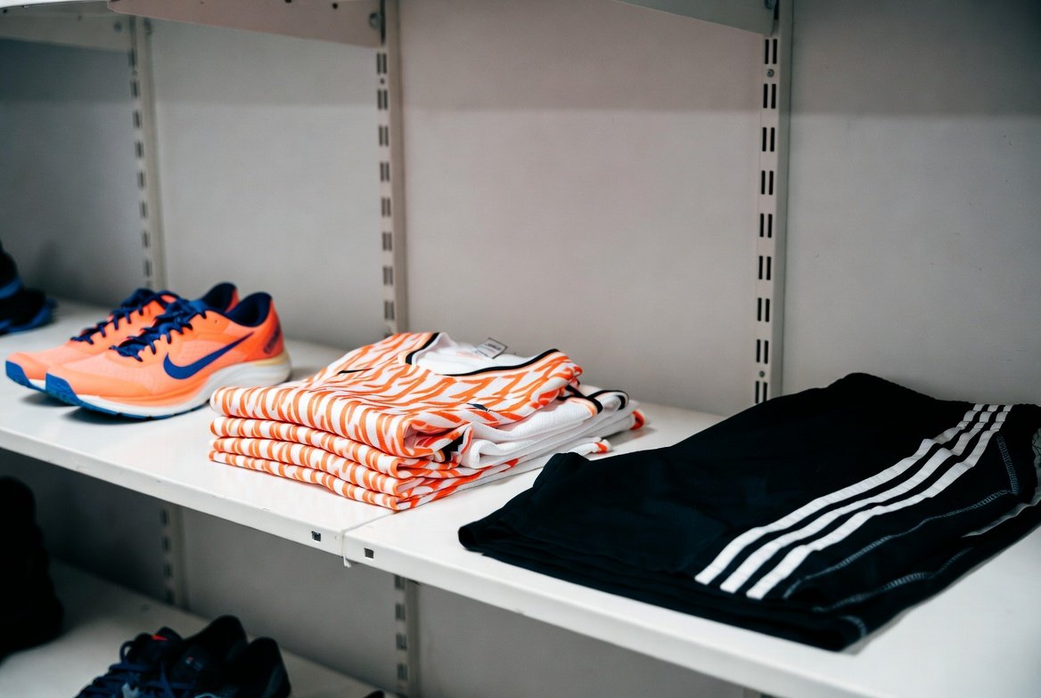 Athletic running shoes, jerseys and training wear neatly arranged on shelves.